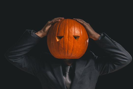 Man with a pumpkin head dressed in a suit against a black background