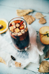 Fototapeta premium Hot mulled wine in a glass with orange slices, anise and cinnamon sticks, star cookies on vintage wood table. Christmas or winter warming drink with recipe ingredients around