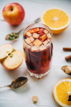 Hot mulled wine in a glass with orange slices, anise and cinnamon sticks, star cookies on vintage wood table. Christmas or winter warming drink with recipe ingredients around