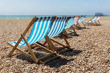 Classic blue, red and white striped empty deckchairs on the beach. The old pier in Brighton in the background