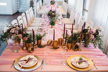 Tables for guests decorated in pink color with flowers, candles, gold vases and eucalyptus