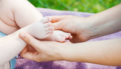 The mother hands are holding the little son feet. Protection and love concept