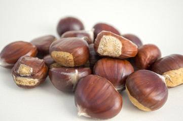 Raw sweet chestnuts scattered on a white background, tasty and healthy brownish nuts