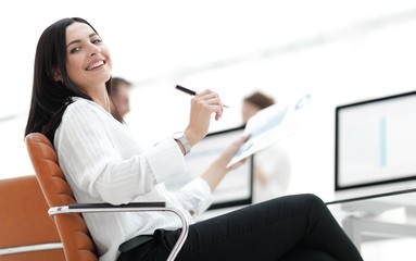 smiling business woman with financial documents sitting at work desk.