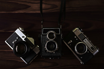 Three old vintage cameras on a wooden table.