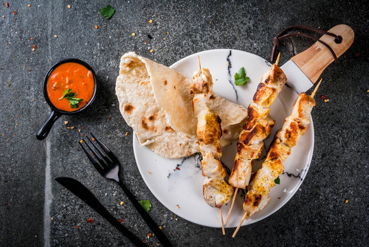 Indian food. Traditional dish spicy chicken tikka masala, butter chicken curry, with indian naan butter bread, spices, herbs. Served in bowl. sauce, on skewers. Stone dark table. copy space top view