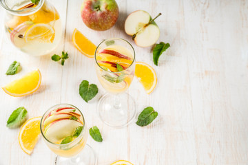 Drinks and cocktails. White autumn sangria with apples, orange, mint and white wine. In glasses for champagne, in a pitcher, on a white wooden table. Copy space top view