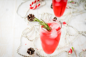 Obraz na płótnie Canvas New Year's, Christmas drinks. Red alcohol cocktail with cranberry, liqueur, rosemary, with ice. On a white table, with Christmas candies, ornaments and pine cones. Copy space