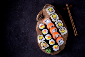 Sushi with wasabi and marinated ginger on an olive board on a black concrete background.