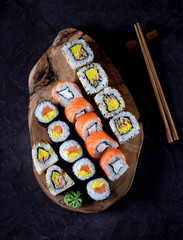 Sushi with wasabi and marinated ginger on an olive board on a black concrete background.