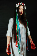 Portrait of a bloody beautiful Asian girl on Halloween. White dress-robe, ethnic wreath of flowers.