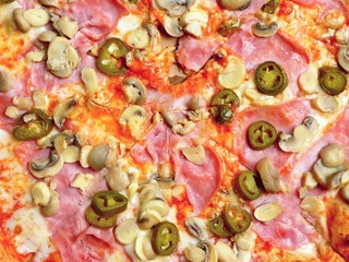 Top view of a pizza with chili peppers, ham and mushrooms. 