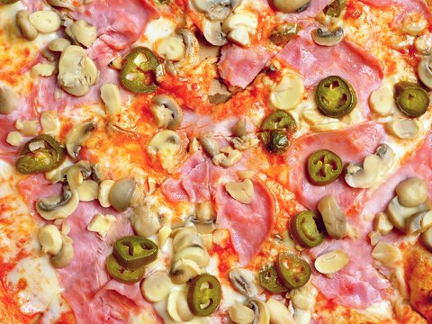 Top view of a pizza with chili peppers, ham and mushrooms. 