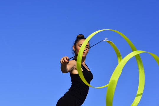 Woman gymnast in black sportswear with green ribbon.