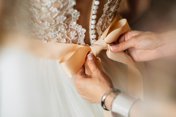 Bride getting ready. Wedding morning. Best friend binding bow on dress.