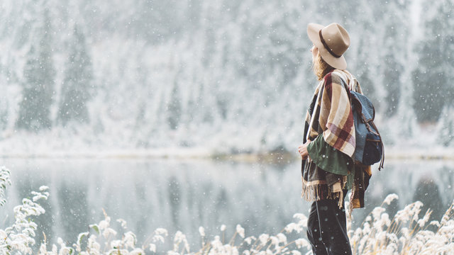Beautiful traveling woman enjoying wilderness in front of stunning mountain lake. Winter is coming, first snowfall. Wanderlust and boho style