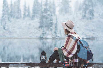 Traveling woman sitting with kerosene lamp in front of amazing frozen landscape. Wearing hat,...