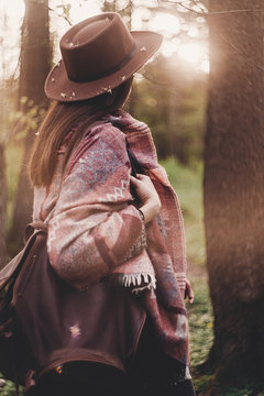 stylish hipster traveler girl in hat with backpack exploring in woods in amazing evening sunshine light. woman looking in sunlight. space for text. atmospheric moment. wanderlust