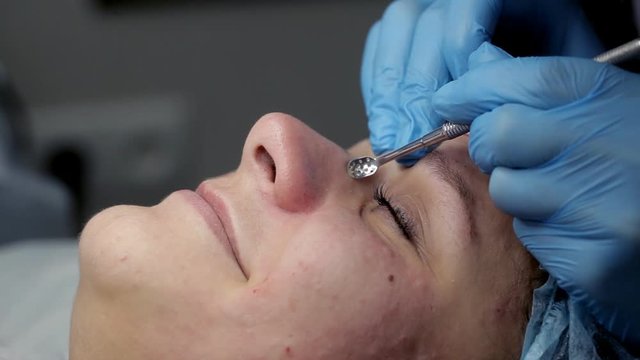 The beautician makes a cleansing of the nose area during the procedure of mechanical facial cleansing