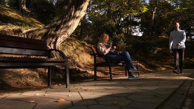4k, slow-motion, girl with a camera sits on a bench in a picturesque place. Passers pass by.