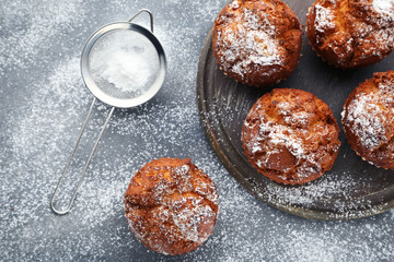 Tasty muffins with cutting board and sieve on grey wooden table