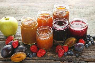 Glass jars with different kinds of jam on wooden table