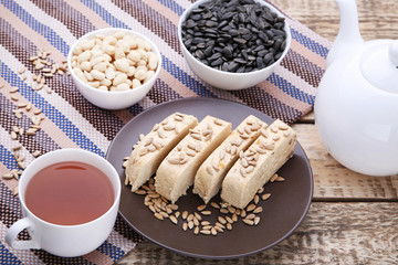 Tasty slices of halva in plate with cup of tea on wooden table