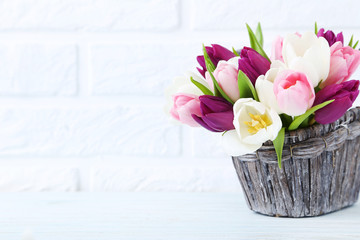 Bouquet of tulips in basket on brick wall background