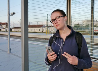 Mädchen mit Musik im Ohr wartet am Bahnhof auf Zug