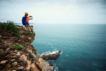 Young woman hiker taking photo with smartphone sit on seaside cliff