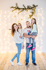 Happy family have fun, fooling around on the background of yellow garlands of lights and bokeh Christmas tree branches. Good New Year spirit. Parents daughters throw confetti, hug, laugh. Copy space