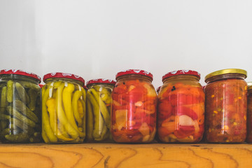 Pickled vegetables in jars, colorful, on a wooden shelf against white background
