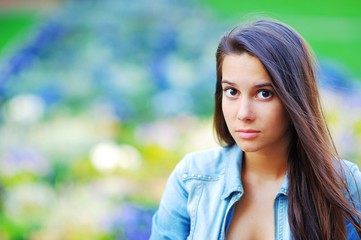 Naklejka premium Portrait of an attractive long haired brunette woman with beautiful sad brown eyes on streets on colorful blurred background, closeup.