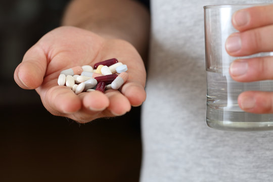 Man hand showing a lot of pills and a glass of water