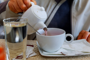 Hands holding a glass brewer in one hand and a cup of tea in another.