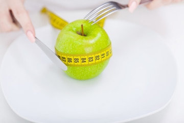 Diet concept, green apple on a white plate, yellow measuring tape, fork, knife, weight loss, healthy diet