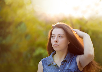 Attractive young woman with long brown hair enjoying hertime in the park with sunset in background.