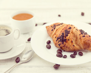 Fresh chocolate croissants and cup of coffee on white rustic wooden table. Healthy breakfast. Traditional food on morning