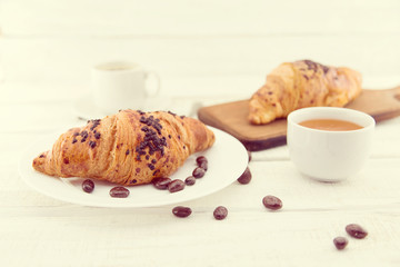 Fresh chocolate croissants and cup of coffee on white rustic wooden table. Healthy breakfast. Traditional food on morning