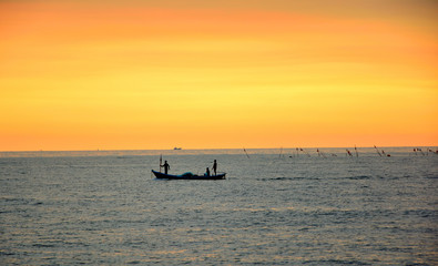 Three fishermen on a small fishing boat go out to fish at sunset.