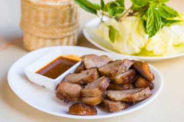 Tasty cut grilled pork with spicy sauce on white dish, This dish eat with sticky rice and fresh vegetable, Thai food