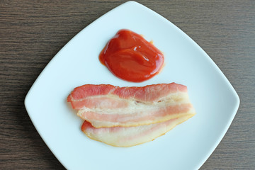 bacon with ketchup on white plate.