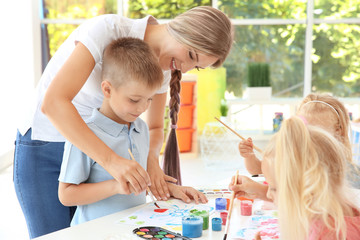 Little boy with teacher at painting lesson in classroom