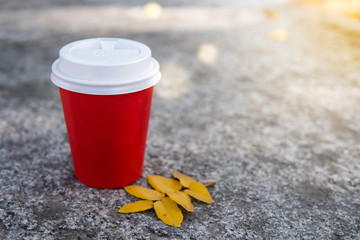 Coffee to go and autumn leaves in sunny day. Coffee takeaway in red cup