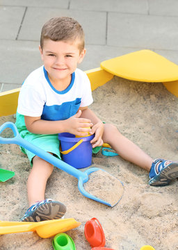 Little boy playing with toys in sand box outdoors