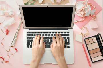 Hands of beauty blogger with modern laptop and different women's items on table