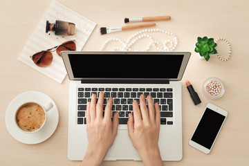 Hands of beauty blogger with modern laptop and different women's items on table