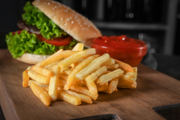 Wooden board with yummy french fries, closeup