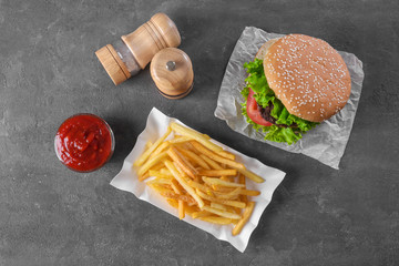 Paper container with yummy french fries and hamburger on table
