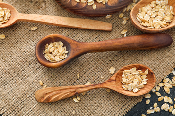 Oatmeal flakes in wooden spoons on sackcloth fabric